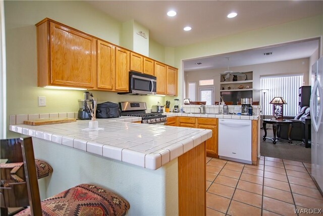 kitchen featuring light tile patterned floors, tile counters, a peninsula, stainless steel appliances, and a sink