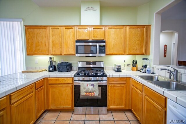 kitchen featuring arched walkways, light tile patterned flooring, stainless steel appliances, a sink, and tile counters