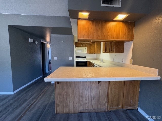 kitchen with brown cabinetry, electric range oven, white microwave, baseboards, and dark wood-style floors