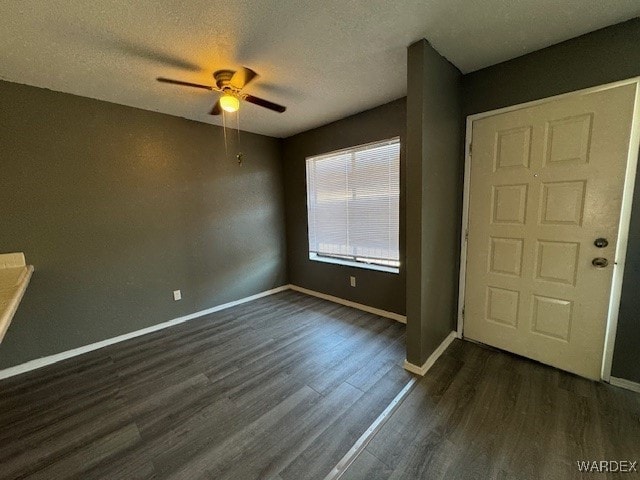 spare room featuring dark wood-type flooring, a textured ceiling, a ceiling fan, and baseboards