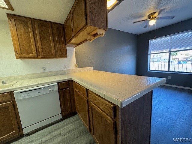 kitchen with tile counters, white dishwasher, light wood-style floors, a peninsula, and ceiling fan