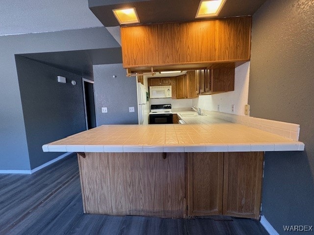kitchen with dark wood finished floors, a peninsula, a textured wall, and white appliances