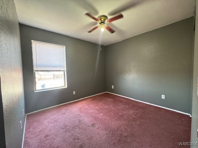 empty room featuring a textured wall, baseboards, dark carpet, and ceiling fan