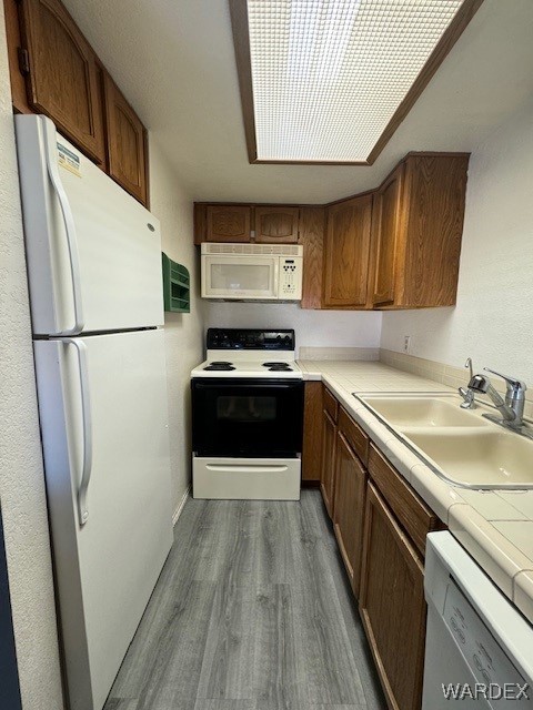 kitchen featuring tile counters, dark wood-style floors, a sink, white appliances, and brown cabinetry