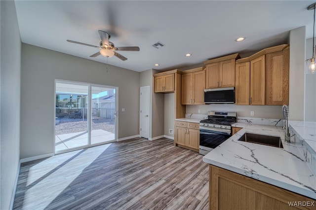 kitchen with hanging light fixtures, light stone countertops, appliances with stainless steel finishes, and a sink