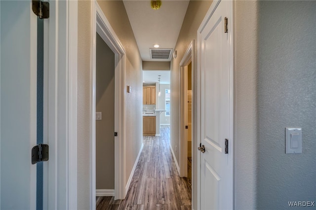 hallway featuring a textured wall, wood finished floors, visible vents, and baseboards