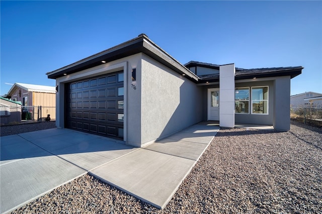 view of front facade featuring concrete driveway, fence, an attached garage, and stucco siding