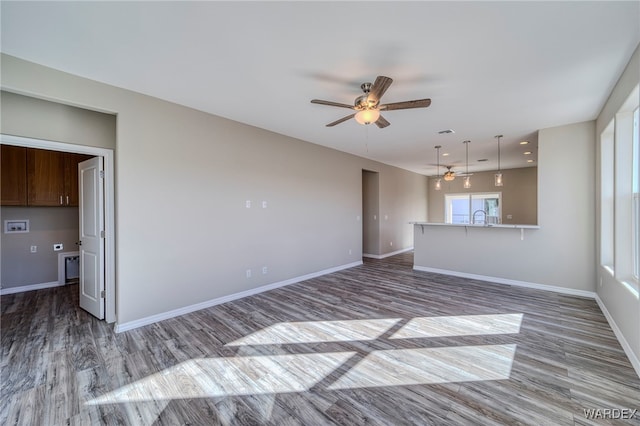 unfurnished living room featuring ceiling fan, a sink, baseboards, and wood finished floors