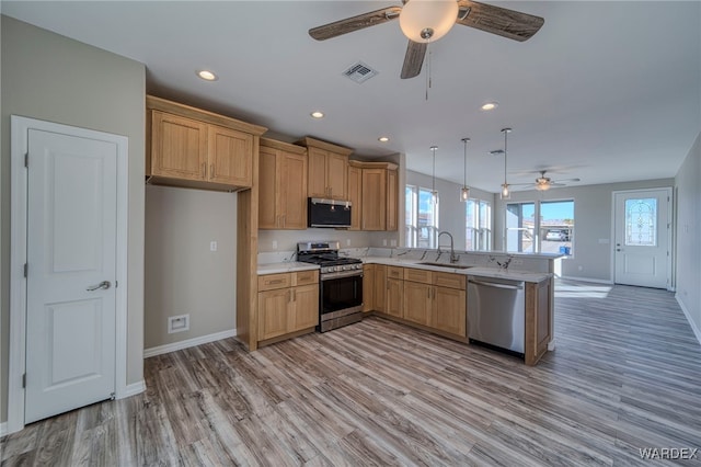 kitchen featuring stainless steel appliances, a peninsula, a sink, light countertops, and decorative light fixtures