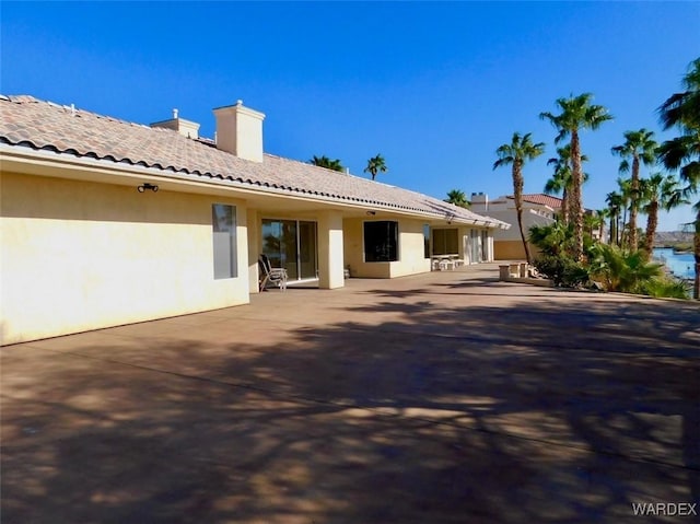 rear view of house with a patio, a chimney, a tiled roof, and stucco siding