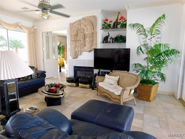 living area featuring crown molding, ceiling fan, and a tiled fireplace