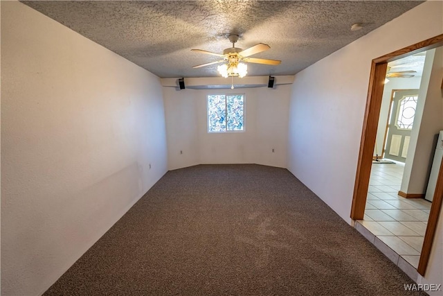 empty room featuring light tile patterned floors, a ceiling fan, a textured ceiling, and light colored carpet