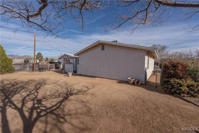 view of side of home with a gate, fence, and stucco siding