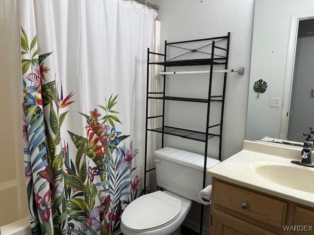 bathroom featuring a textured wall, shower / tub combo with curtain, vanity, and toilet