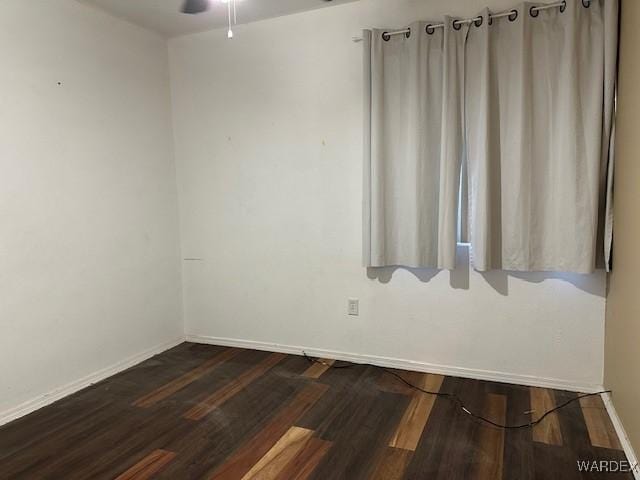 spare room featuring a ceiling fan, baseboards, and dark wood-type flooring