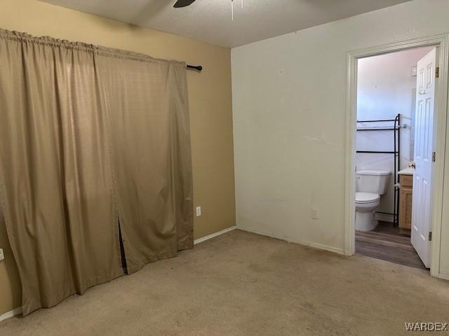 unfurnished bedroom featuring ensuite bathroom, ceiling fan, carpet flooring, and baseboards