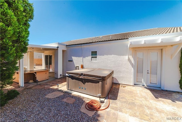 rear view of property featuring stucco siding, a patio area, a tile roof, and a hot tub