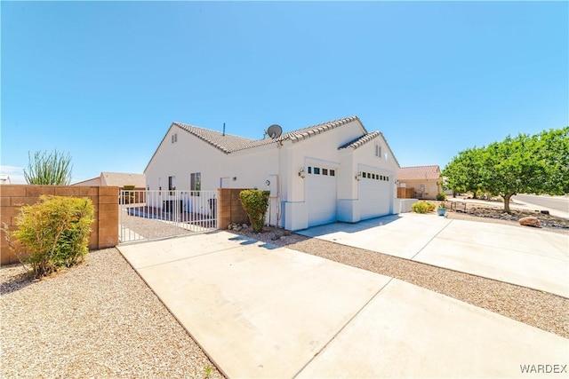 view of side of home with a garage, fence, driveway, a gate, and stucco siding