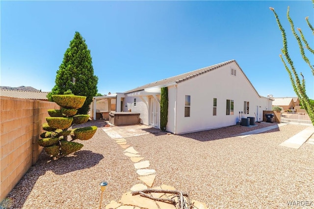 rear view of property featuring a patio, stucco siding, a fenced backyard, and a hot tub