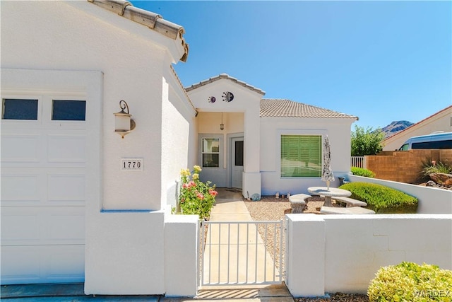 property entrance with an attached garage, fence, a tiled roof, a gate, and stucco siding