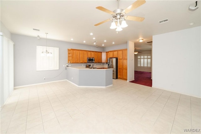 kitchen featuring a peninsula, light countertops, appliances with stainless steel finishes, brown cabinetry, and pendant lighting