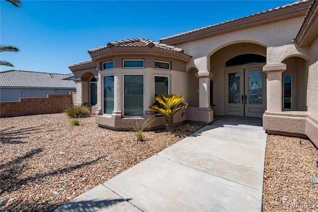 property entrance featuring stucco siding, fence, and french doors