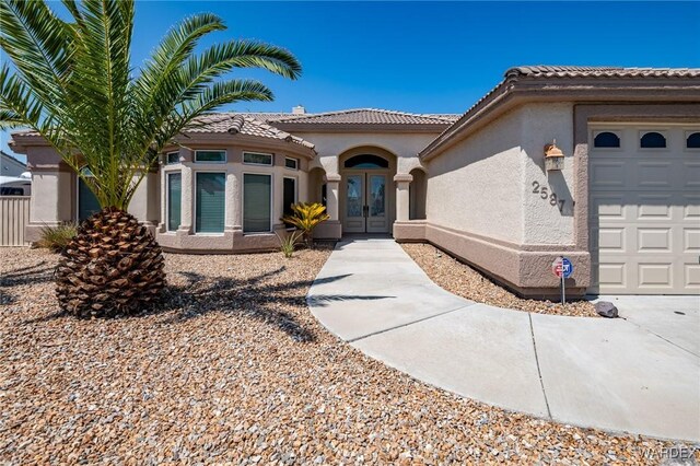 view of front of property with a tiled roof, french doors, an attached garage, and stucco siding