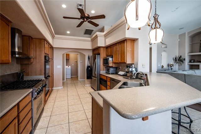 kitchen featuring arched walkways, appliances with stainless steel finishes, wall chimney range hood, a kitchen bar, and a sink