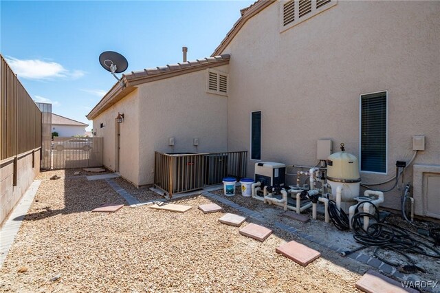 rear view of property featuring a gate, fence, and stucco siding