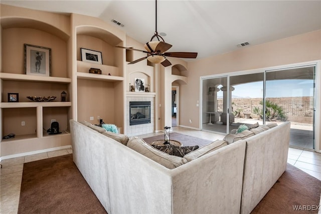 tiled living room featuring lofted ceiling, built in shelves, a fireplace, visible vents, and a ceiling fan