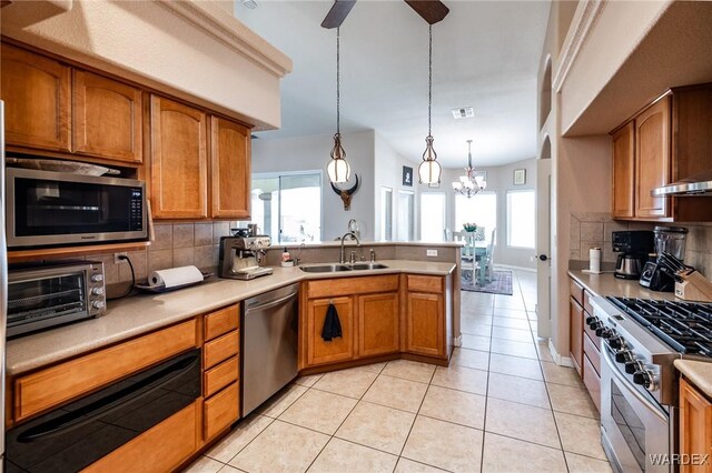 kitchen featuring stainless steel appliances, a sink, light countertops, brown cabinets, and pendant lighting