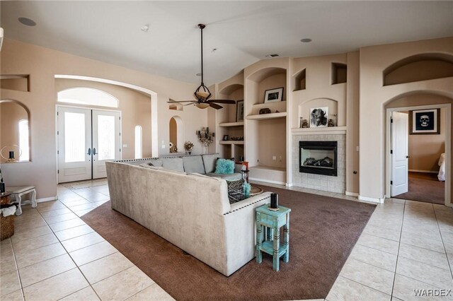 living room featuring built in shelves, french doors, light tile patterned flooring, vaulted ceiling, and a tile fireplace