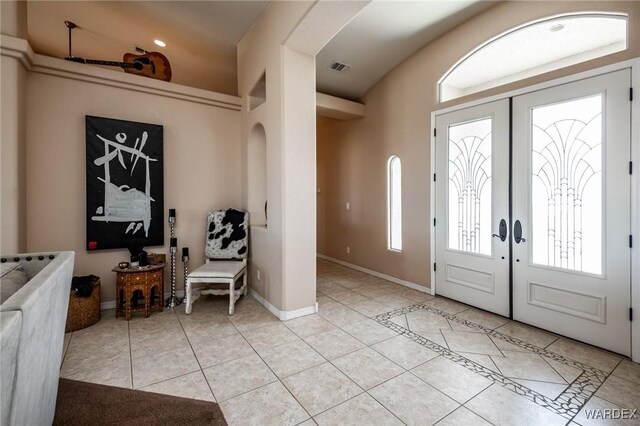 foyer featuring light tile patterned floors, visible vents, baseboards, arched walkways, and french doors