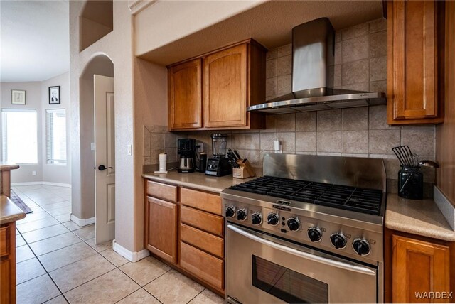 kitchen with decorative backsplash, brown cabinets, light countertops, wall chimney range hood, and stainless steel range with gas cooktop