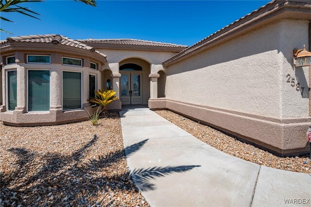 property entrance with a tiled roof, french doors, and stucco siding