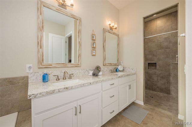 bathroom with double vanity, a tile shower, and a sink