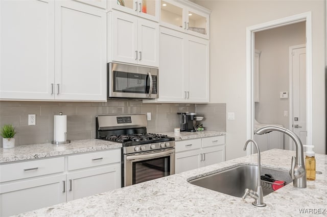 kitchen featuring white cabinets, decorative backsplash, glass insert cabinets, stainless steel appliances, and a sink