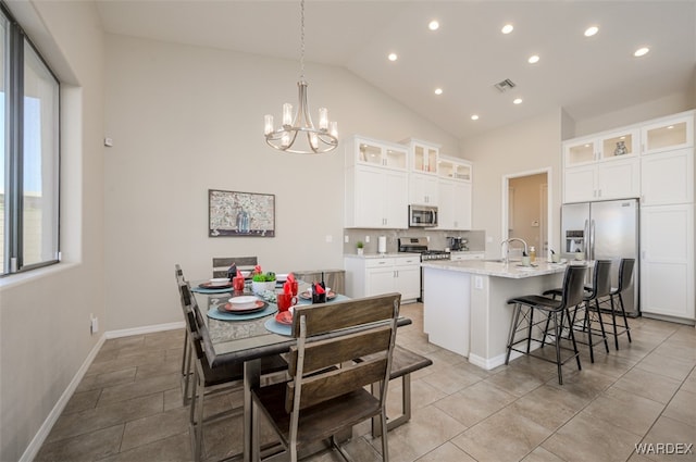 kitchen featuring stainless steel appliances, hanging light fixtures, glass insert cabinets, a kitchen island with sink, and white cabinets