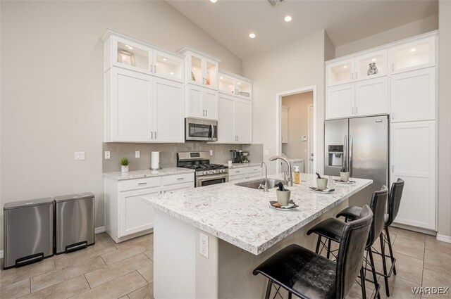 kitchen featuring stainless steel appliances, white cabinets, glass insert cabinets, and a center island with sink