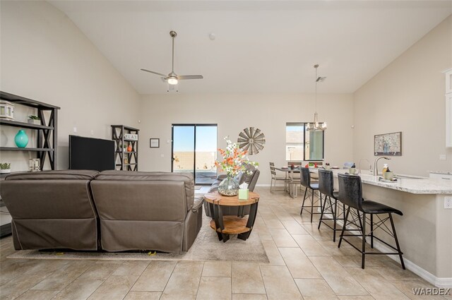 living room featuring light tile patterned floors, baseboards, high vaulted ceiling, and ceiling fan with notable chandelier