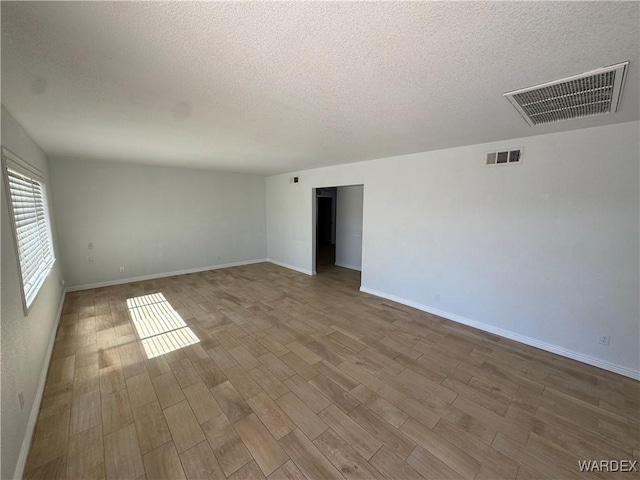 spare room with baseboards, a textured ceiling, visible vents, and wood finished floors