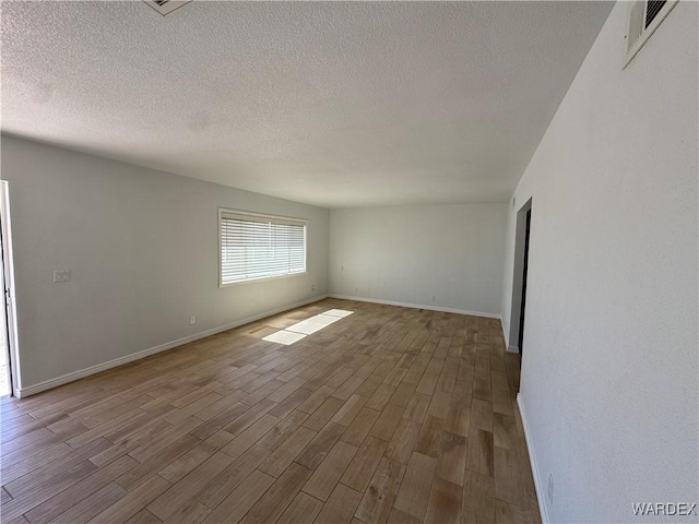 unfurnished room featuring dark wood-style floors, baseboards, visible vents, and a textured ceiling