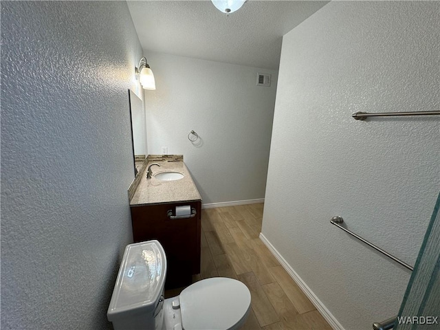 bathroom featuring a textured wall, wood finished floors, vanity, visible vents, and baseboards