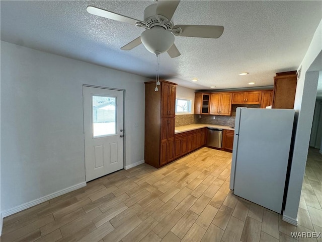 kitchen with light countertops, stainless steel dishwasher, backsplash, freestanding refrigerator, and brown cabinets