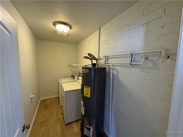 laundry area with light wood-style flooring, electric water heater, a textured ceiling, washer and dryer, and laundry area