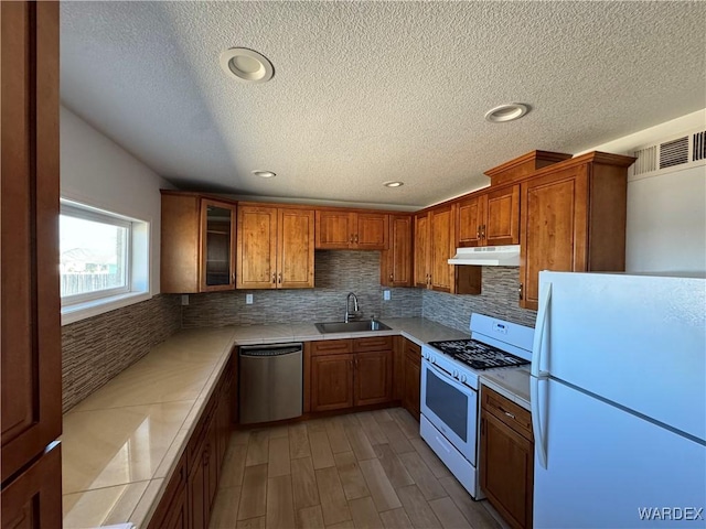 kitchen featuring brown cabinets, light countertops, a sink, white appliances, and under cabinet range hood