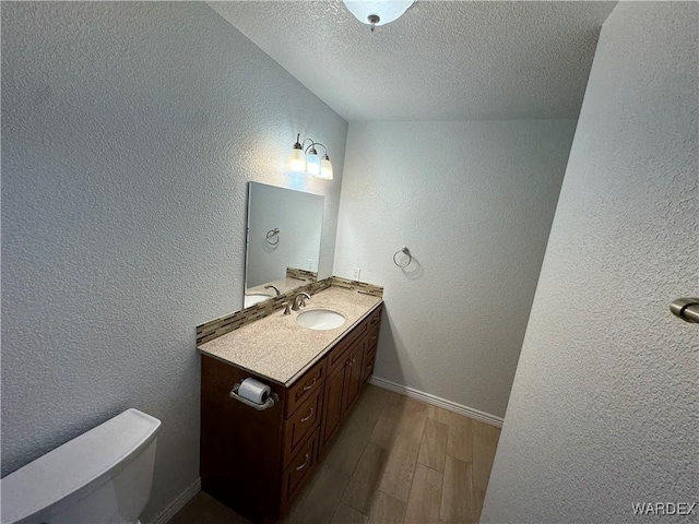 bathroom featuring toilet, vanity, wood finished floors, and a textured wall