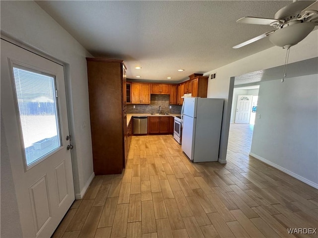 kitchen with light wood finished floors, light countertops, decorative backsplash, a sink, and white appliances