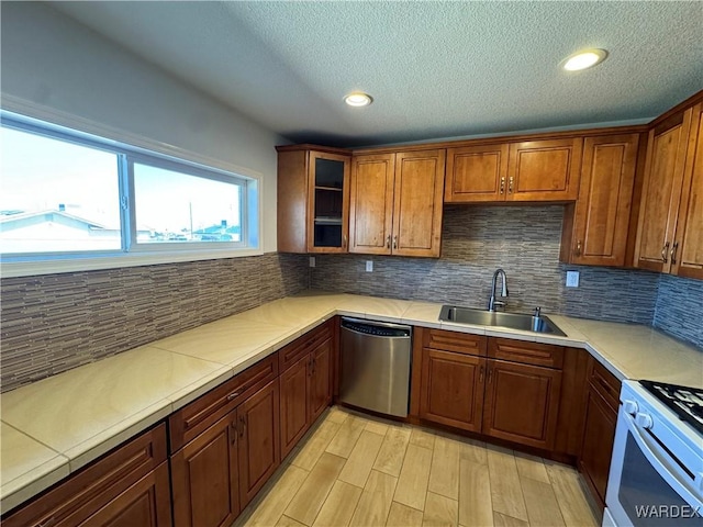 kitchen featuring dishwasher, glass insert cabinets, light countertops, white gas stove, and a sink