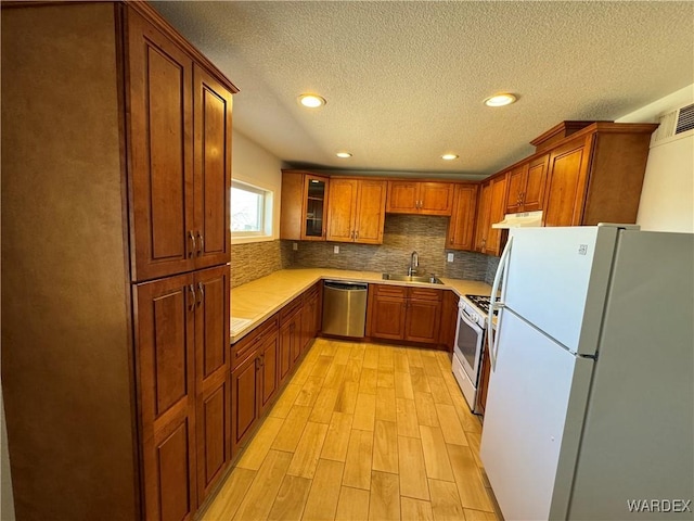 kitchen with white appliances, a sink, light countertops, light wood-type flooring, and backsplash